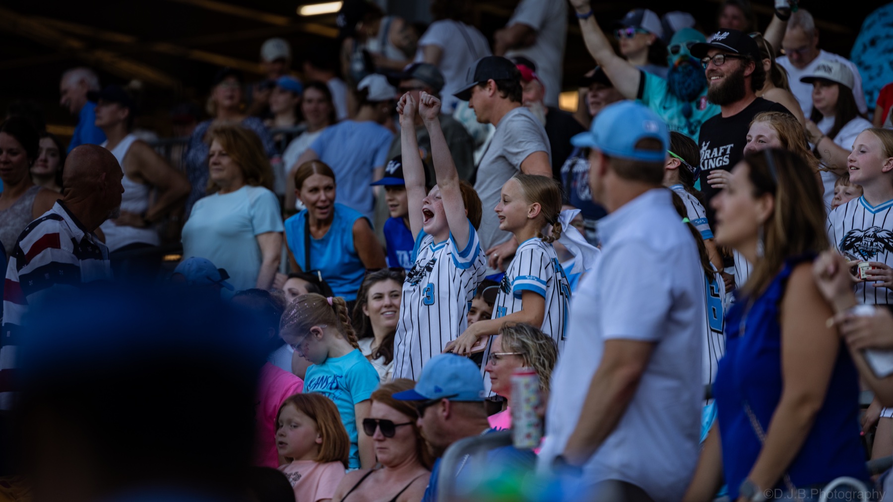 Young softball fans cheering from the stands with their arms raised