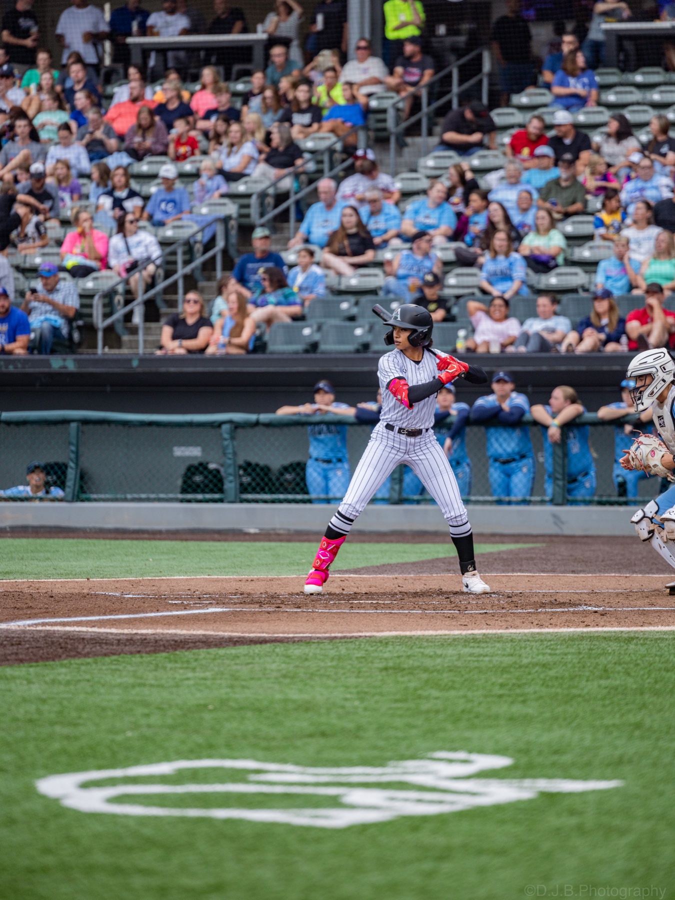 A softball batter waits at the plate in front of a stadium crowd