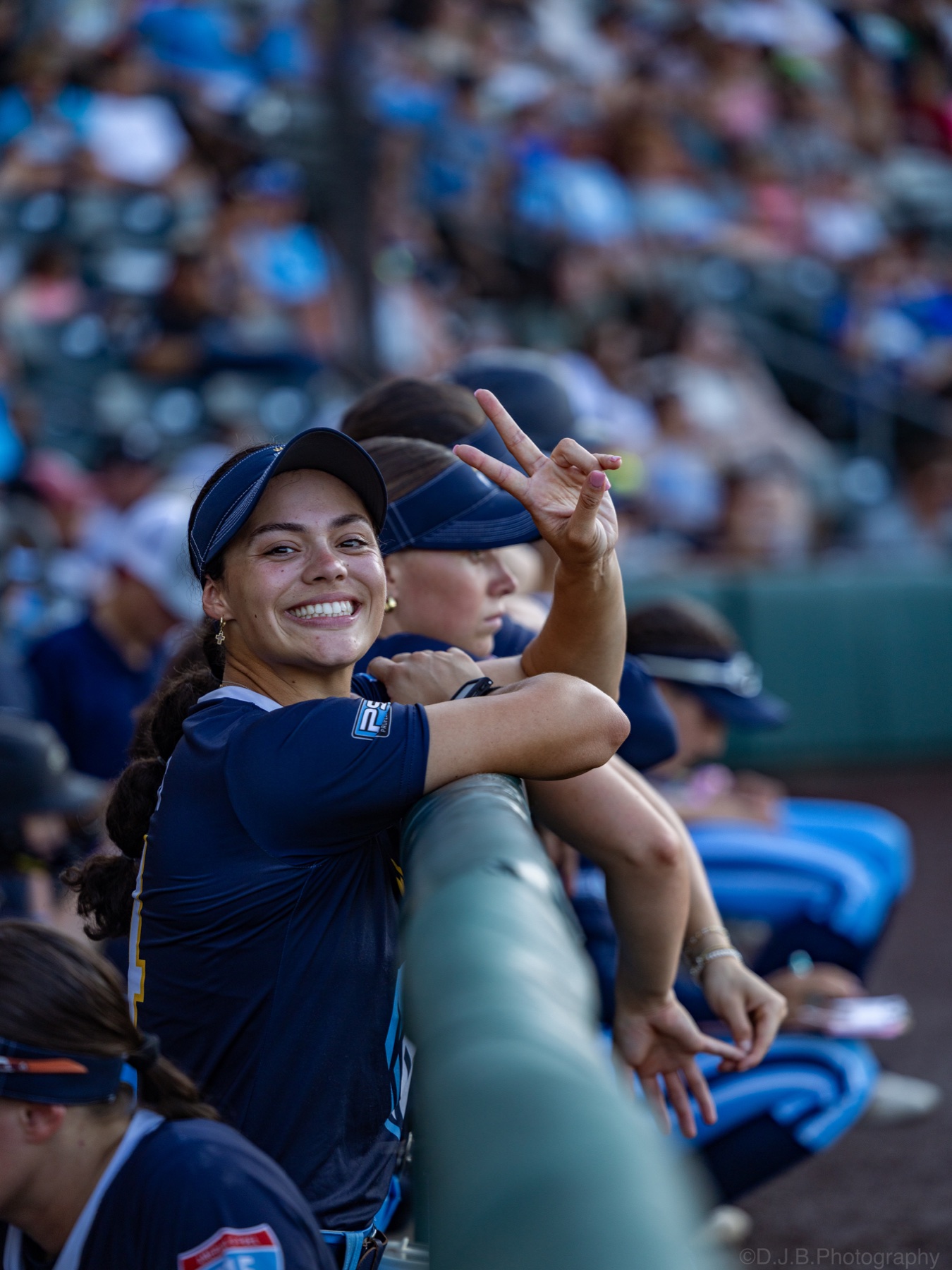 A smiling softball player flashes a peace sign from the dugout